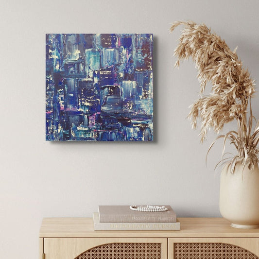 Abstract blue and purple painting on a wall above a wooden cabinet with books and a vase. samhain no. 2