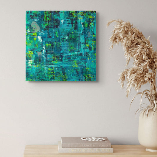 Abstract painting in teal and green on a wall above a wooden cabinet with books and a vase.