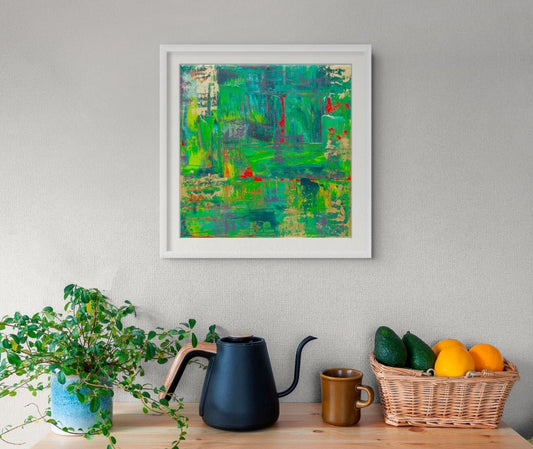 A framed abstract painting with vibrant green, blue, and red brushstrokes hangs on a light gray wall above a wooden shelf styled with a potted plant, a black kettle, a brown mug, and a wicker basket of fruit. Samhain no. 3 limited edition print by Julie Bevan