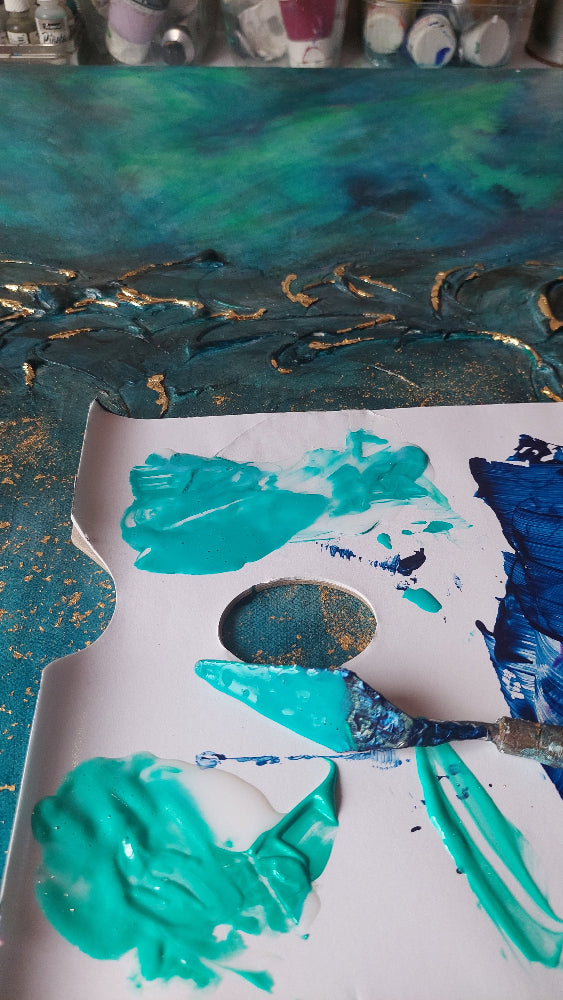 A close-up of a white artist palette with thick, textured paint in turquoise, deep blue, and gold flecks, with paint tubes blurred in the background. Equinox, Original Canvas Painting by Julie Bevan