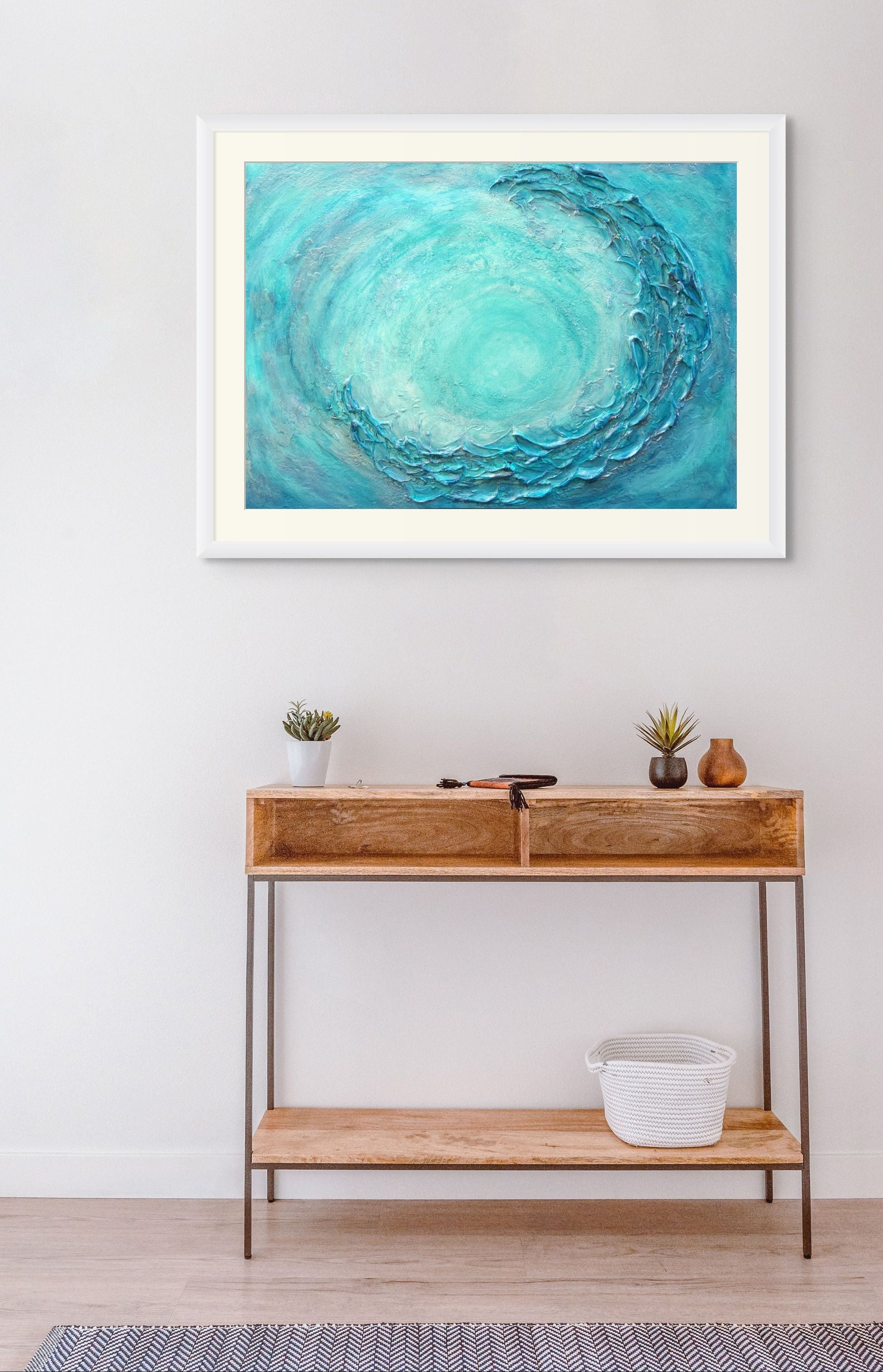 Framed abstract artwork with a blue circular design on a wall above a wooden console table.