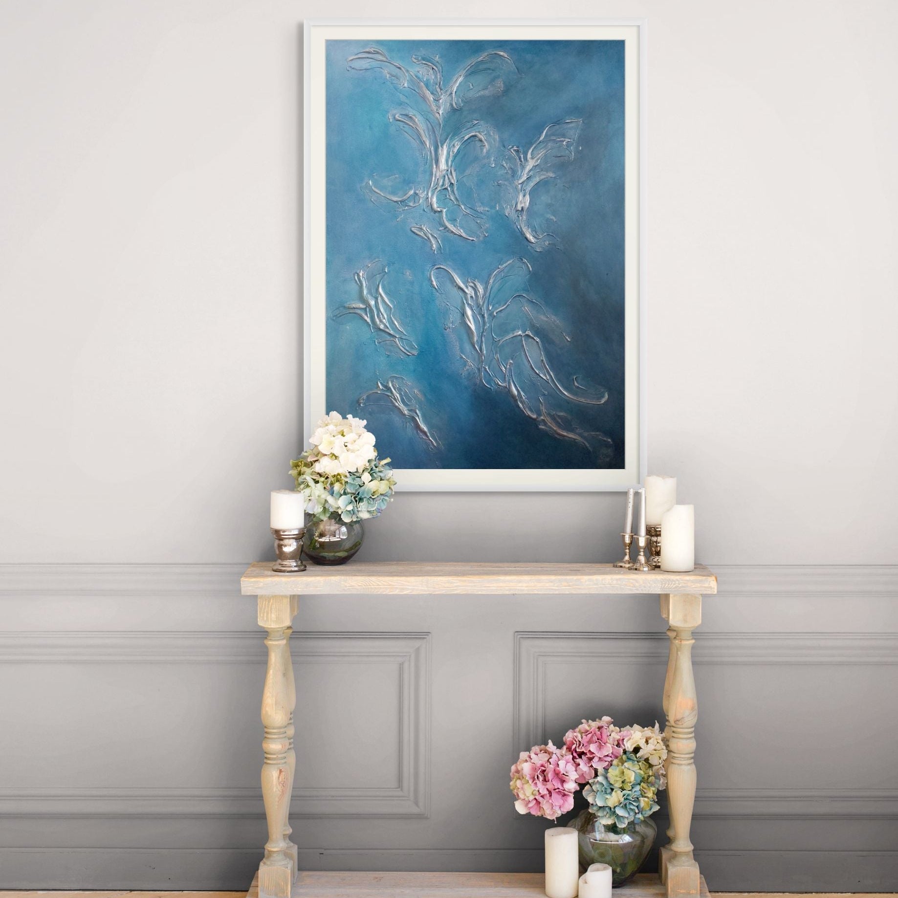 Decorative table with flowers and candles against a gray wall with a large blue abstract limited edition print artwork.