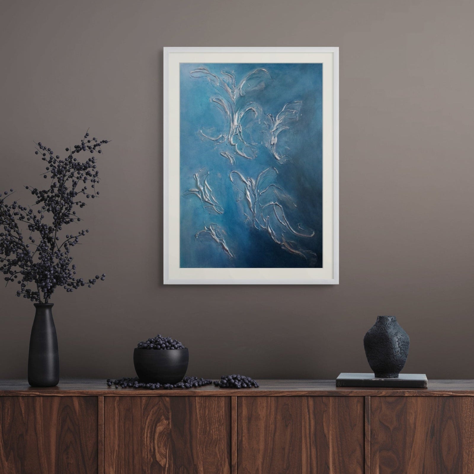 Wooden sideboard with decorative items and a framed blue abstract limited edition print artwork on a gray wall.