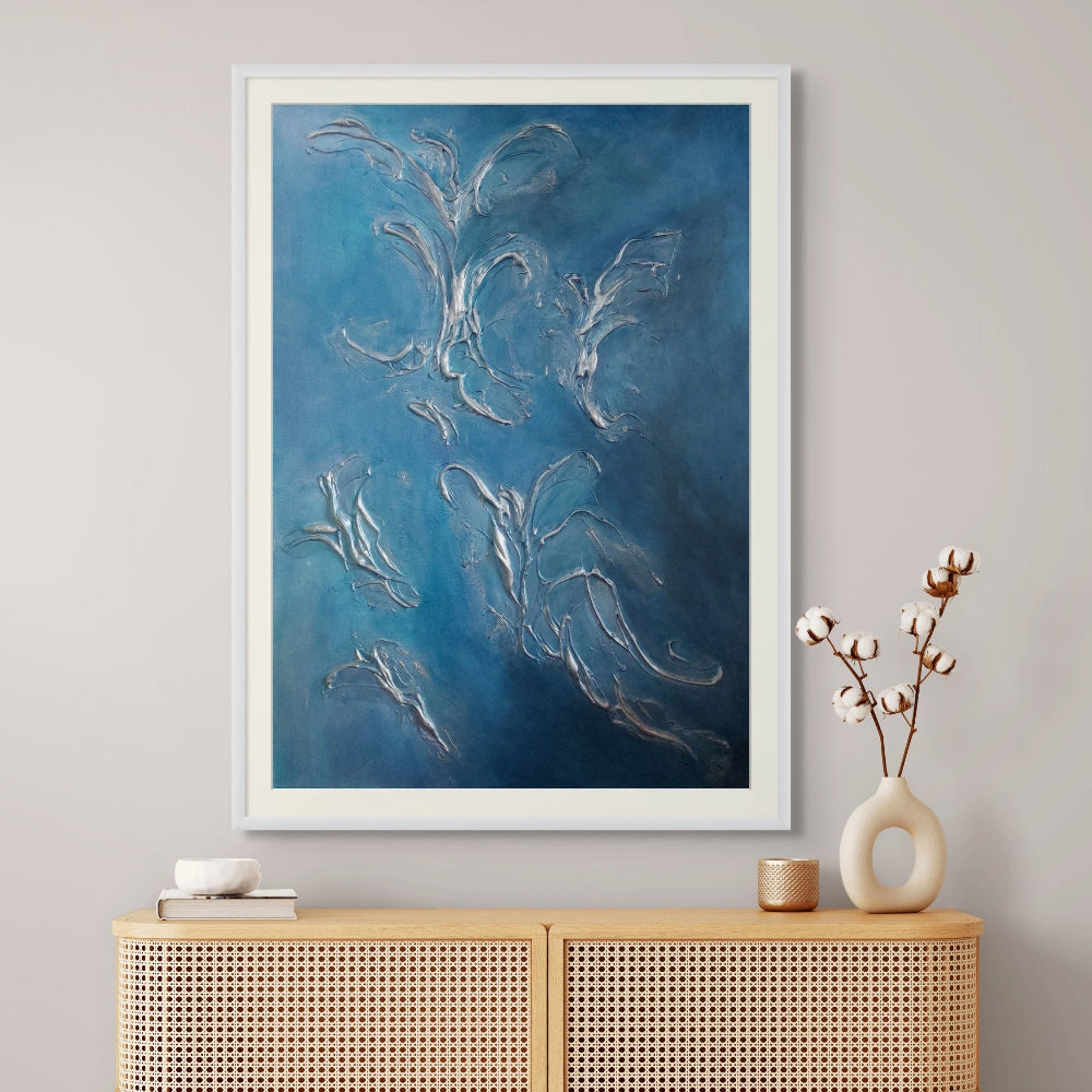 Framed blue abstract limited edition print artwork on a wall above a wooden cabinet with decorative items.