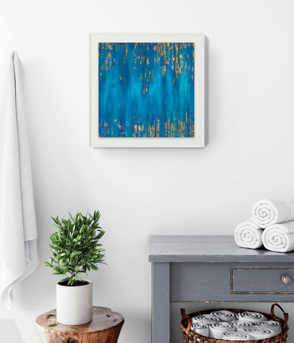 Framed abstract art piece on a wall above a plant and towels. Blue Zone fine art Print on museum grade Paper blue, turquoise and gold. Living room art