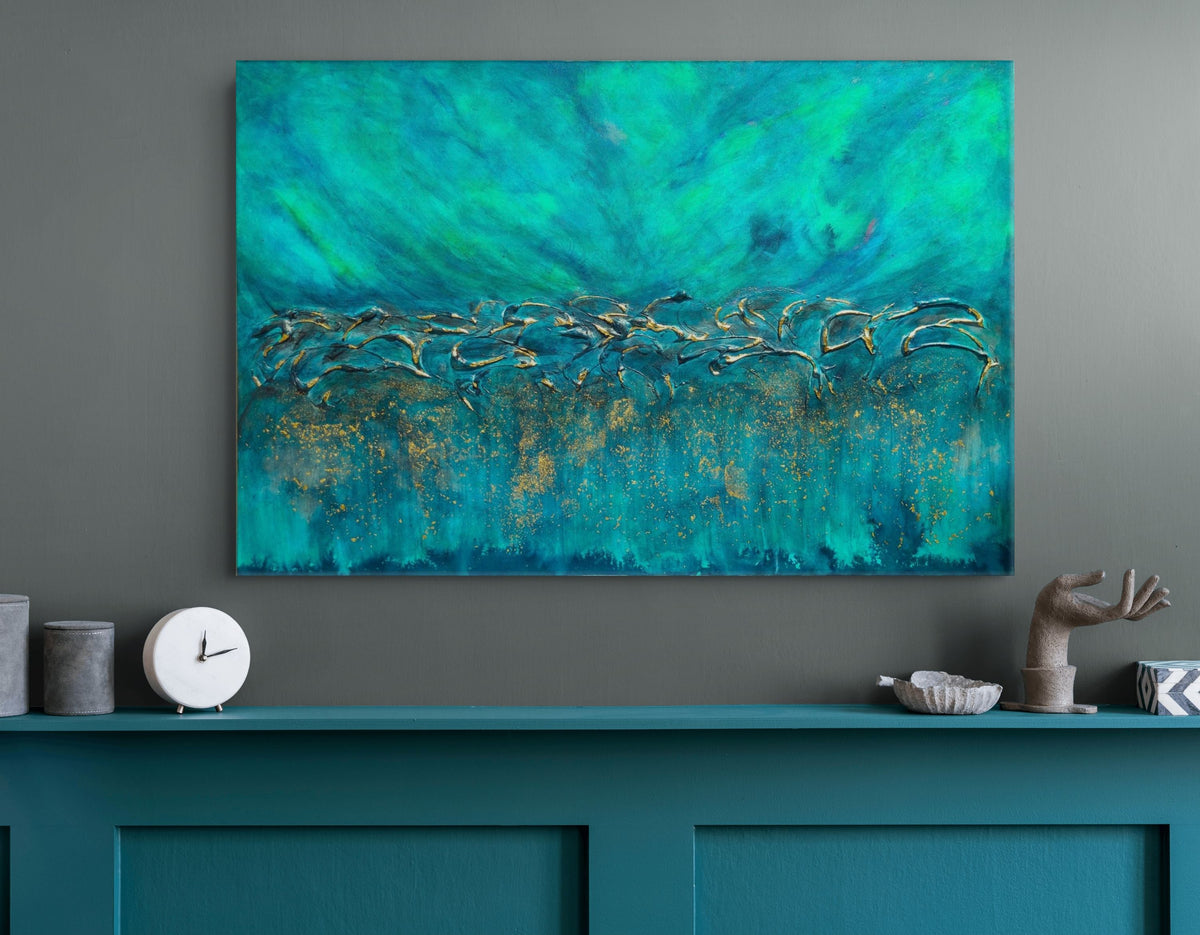 A large abstract canvas painting featuring vibrant teal, turquoise, and gold brushstrokes, displayed on a dark gray wall above a matching teal cabinet with decorative objects. Equinox, Original Canvas Painting by Julie Bevan