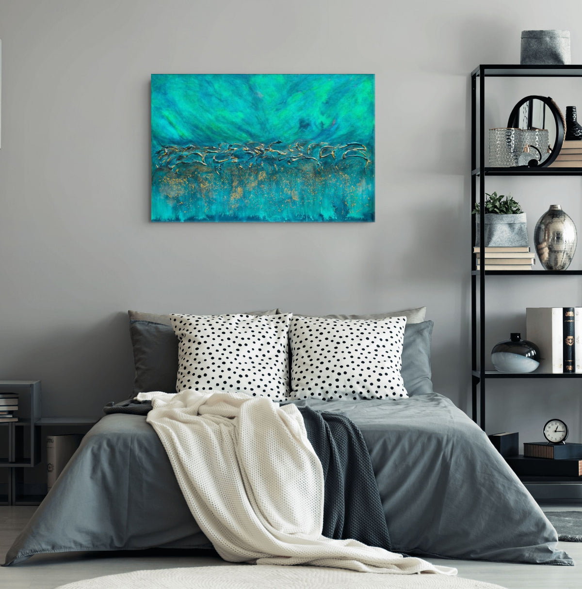 A square abstract canvas print with vibrant teal, turquoise, and gold brushstrokes, displayed on a light gray wall above a modern gray bed with patterned pillows and a cream throw blanket. Equinox, Original Canvas Painting by Julie Bevan