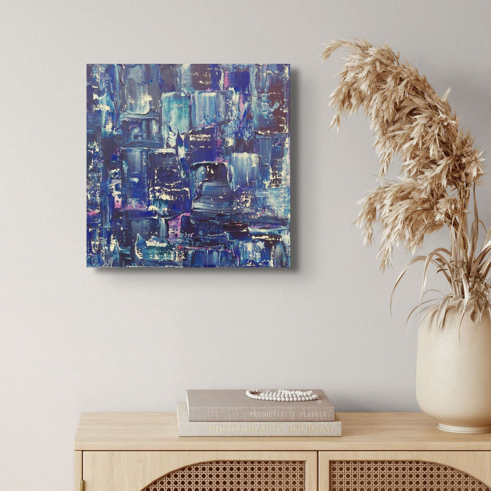 Abstract blue and purple painting on a wall above a wooden cabinet with books and a vase. samhain no. 2