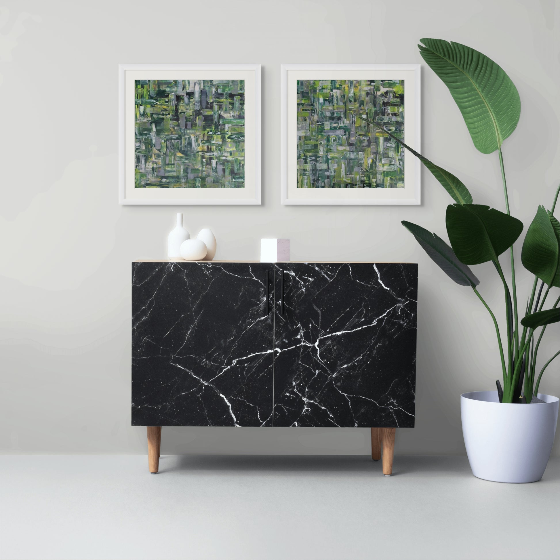 Black marble cabinet with two abstract art pieces and a plant on a light gray background