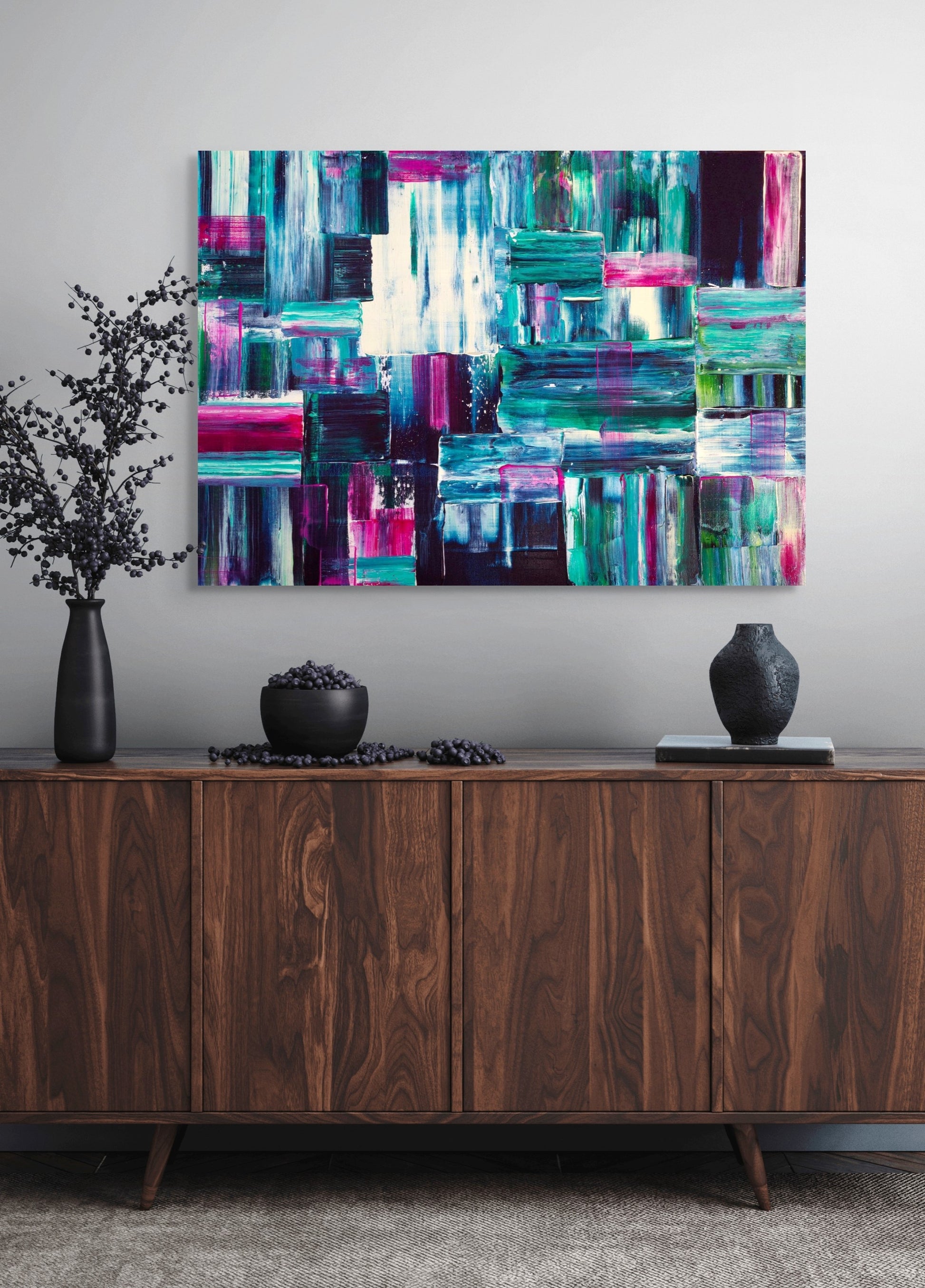 Abstract colorful painting on a wall above a wooden cabinet with decorative items.