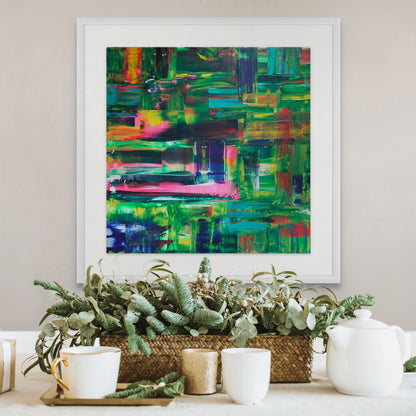 Colorful abstract painting in a white frame above a decorative table setting with plants and teacups.